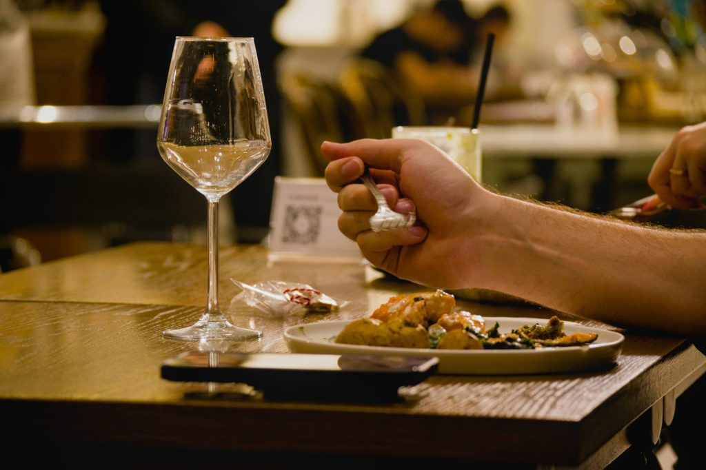 A person eating food at a table with wine.