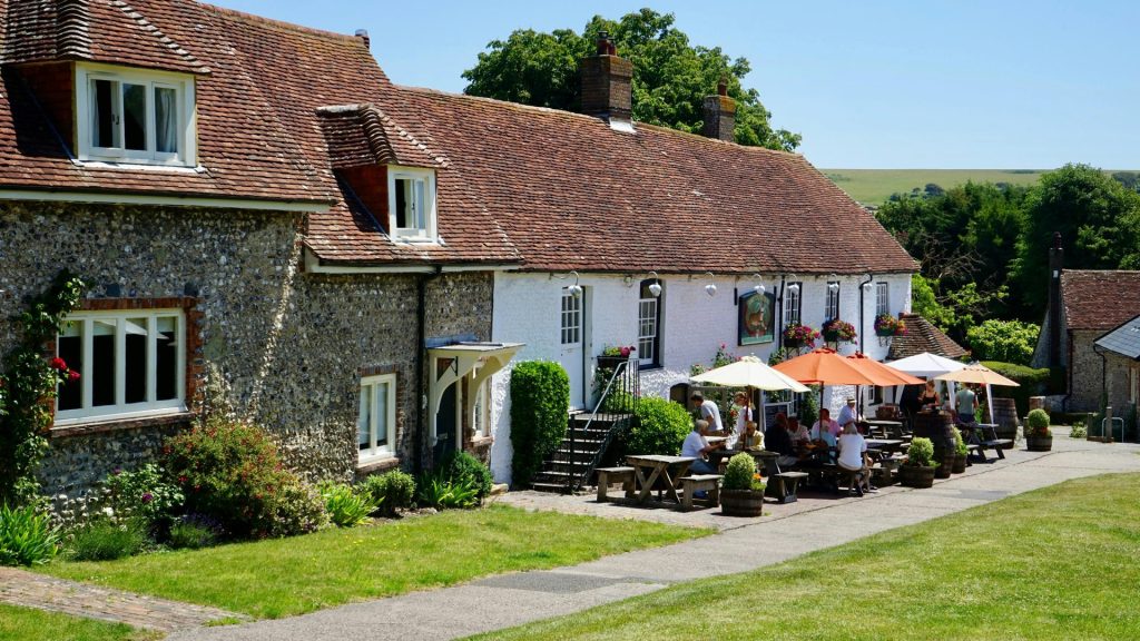 Charming countryside house with people enjoying an outdoor cafe area on a sunny day.
